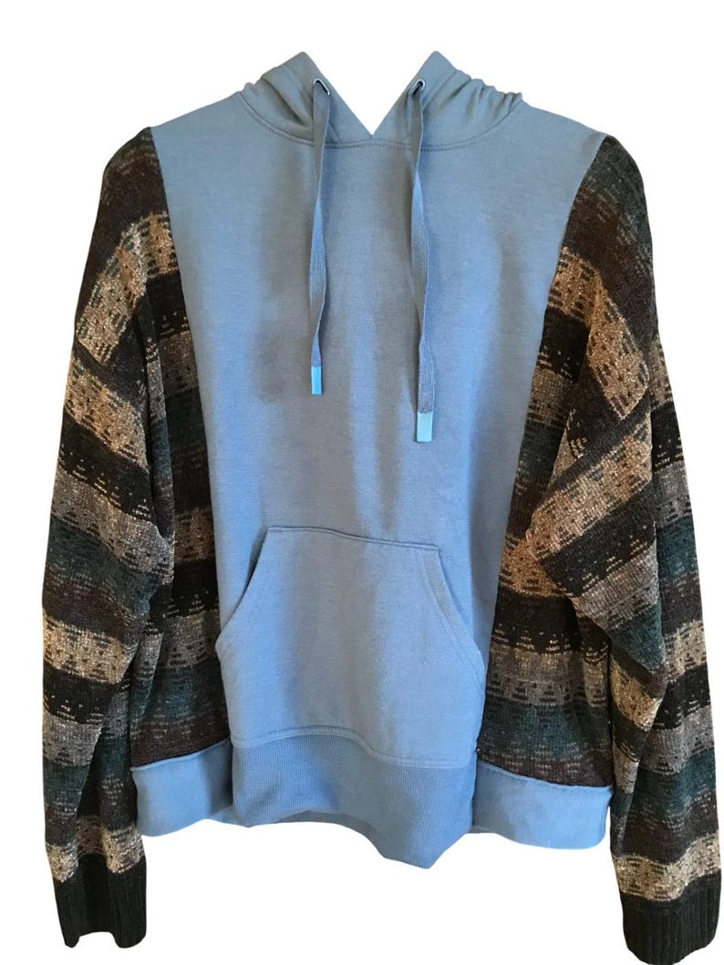 May include: A long-sleeve hoodie featuring a solid light blue center panel with a matching hood and drawstring, contrasted by sleeves and side panels patterned with horizontal stripes in shades of brown, dark green, and tan with a ribbed hem.