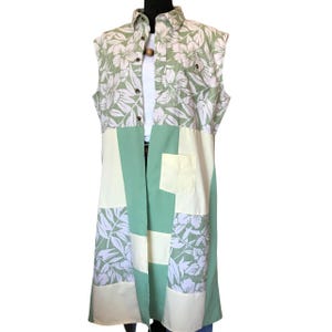 May include: A long, sleeveless, green and white floral patterned shirt with a button-up front and a patch pocket on the front.