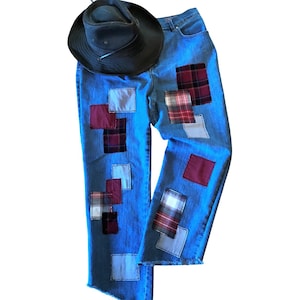 May include: Light blue denim jeans with colorful patchwork and a dark gray hat. The jeans feature various square patches in shades of red, blue, and plaid patterns. The hat is a dark gray, wide-brimmed style.