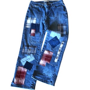 May include: Blue denim jeans with a patchwork design featuring squares of plaid and denim fabric in shades of blue, red, and white.