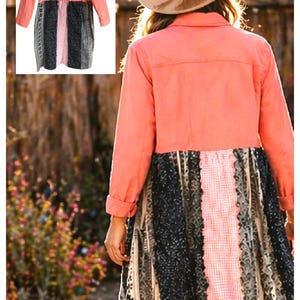 May include: A coral-colored long-sleeve jacket with a patchwork skirt. The skirt features a central pink panel flanked by black and gray patterned sections. The jacket has button closures and a collared neckline. The outfit is worn outdoors.