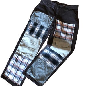 May include: Dark brown pants with patchwork details. The patches include various plaid patterns and solid fabrics in shades of blue, white, and tan. The pants have a button and zipper closure and a pocket.