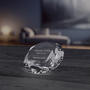 May include: A clear crystal paperweight shaped like a diamond with the text "Loudes & Eric June 28, 2024 Congratulations!" engraved on it.