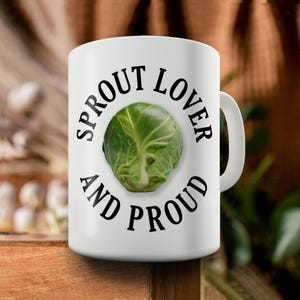 May include: White ceramic mug with a black graphic that says "Sprout Lover and Proud" with a green brussels sprout in the centre.