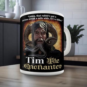 May include: White ceramic mug featuring Tim the Enchanter from Monty Python and the Holy Grail. The mug has a black background with the character's face, horns, and the text "Tim The Enchanter" in a stylized font. A quote is also included.