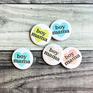 May include: Five heart-shaped buttons with the text "boy mama" in black lettering. The buttons are in various colors: yellow, blue, beige, pink, and light blue.