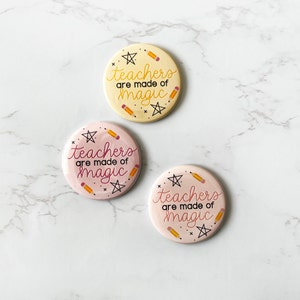 May include: Three round pink and yellow buttons with the text "teachers are made of magic" and a design of stars and pencils.