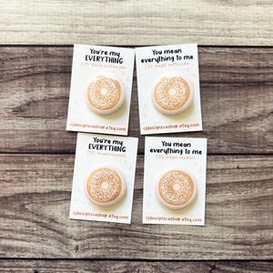 Könnte beinhalten: Vier weiße Karten mit einem Bagel-Design und dem Text "You're my EVERYTHING 1.25" bagel button pin" und "You mean everything to me 1.25" bagel button pin". Die Karten liegen auf einer Holzoberfläche.