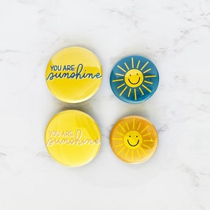 May include: Four round yellow and blue buttons with a sun and the text "You are sunshine" on them.