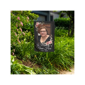 May include: A black garden flag with a gold frame and pink floral accents. The flag features a photo of a woman and the text "In Memory of Name Here Date - Date".