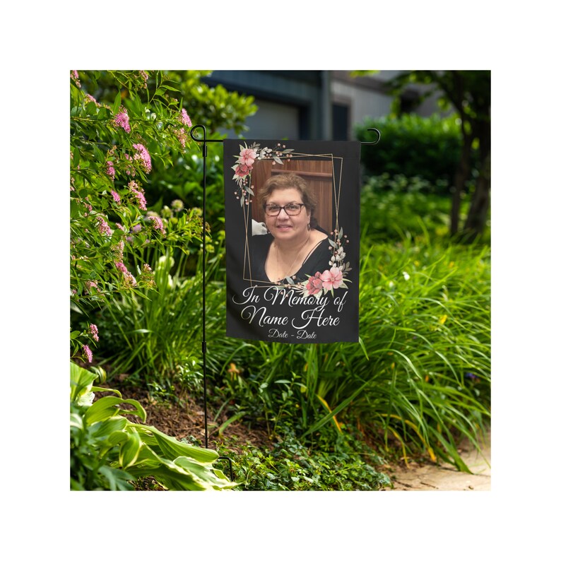 May include: A black garden flag with a gold frame and pink floral accents. The flag features a photo of a woman and the text "In Memory of Name Here Date - Date".