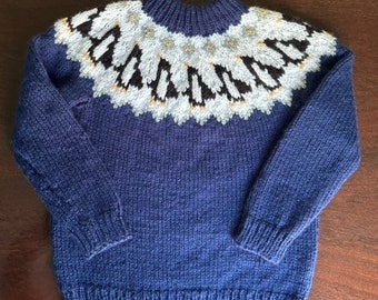 Delightful hand knitted child's jumper in navy blue with penguins dancing around the yolk.