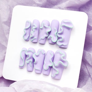 May include: Set of ten lavender-colored fake nails with a light green ruffled design.