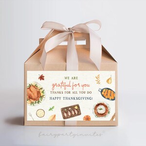 Puede incluir: Una caja de regalo de cartón marrón con una cinta de satén blanca. La caja tiene una etiqueta que dice "We are grateful for you. Thanks for all you do! Happy Thanksgiving!" La etiqueta tiene una ilustración de acuarela de una cena de Acción de Gracias con un pavo, guarniciones y postres.