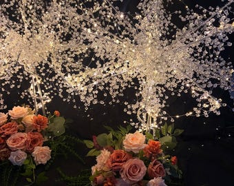 May include: Two decorative light-up trees featuring clear crystal-like beads on thin wire branches, illuminated by small warm white LED lights. Each tree base is adorned with a cluster of artificial roses in shades of dusty pink and terracotta.