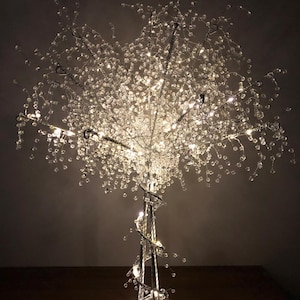 May include: A silver crystal tree with white lights. The tree is made of wire and has a spiral base.