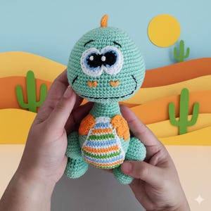 May include: A crocheted dinosaur doll in shades of green, orange, and blue. The dinosaur has large, expressive eyes and a striped belly. The doll is handmade and appears soft and cuddly, perfect for a child's toy or nursery decor.