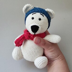 May include: White crocheted polar bear wearing a blue hat and a red scarf.