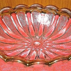 Pode incluir: Uma tigela de vidro transparente com uma borda festonada e um padrão radiante decorativo. A tigela tem uma borda dourada.