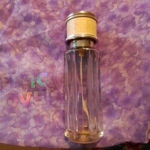 May include: A clear glass bottle with a silver and white cap. The bottle has a textured surface and is empty.