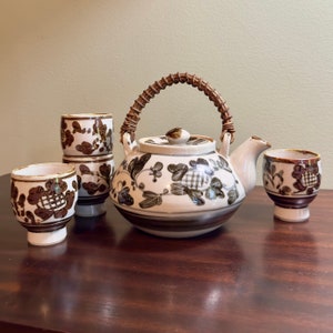 May include: A brown and white ceramic teapot with a woven handle and floral design, along with four matching teacups.
