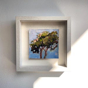 Può includere: Un dipinto a olio quadrato di un albero con fogliame verde e marrone su un cielo azzurro, caratterizzato da spesse pennellate a impasto. L'opera è racchiusa in una cornice di legno testurizzata di colore chiaro con un montaggio profondo.