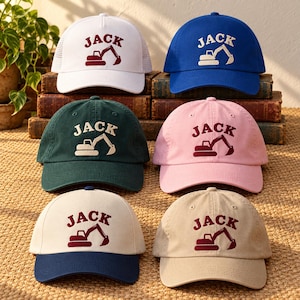 May include: Six baseball caps in white, blue, dark green, pink, cream with navy brim, and tan. Each cap features the name JACK embroidered in an arch above a graphic of an excavator. The white cap has a mesh back, while the others are solid fabric.