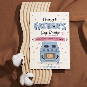 May include: A Father's Day greeting card with the text "Happy Father's Day, Daddy!" and "From your little bun in the oven!" A blue oven graphic with a smiling bun is featured. Pink hearts and stars decorate the card.