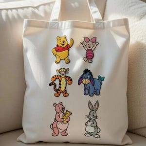 May include: Off-white canvas tote bag featuring colorful cartoon illustrations of Winnie the Pooh and friends. The bag has two handles and is made of a sturdy fabric. The characters include Winnie the Pooh, Piglet, Tigger, Eeyore, Kanga, and Rabbit.