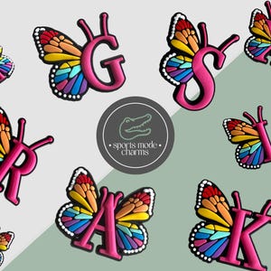 Puede incluir: Amuletos con forma de mariposa rosa con las letras A, G, K, L, R, S y X. Las alas de la mariposa presentan un diseño de arcoíris colorido. Los amuletos son probablemente para zapatos o accesorios, con un logotipo "sports mode charms."