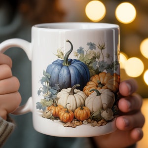 May include: White ceramic mug with a colorful autumn-themed design featuring pumpkins, leaves, and vines. The pumpkins are blue, orange, and white.