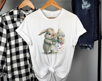 Puede incluir: Camiseta blanca con una ilustración de acuarela de un conejo marrón sosteniendo un ramo de flores rosas, naranjas y amarillas.