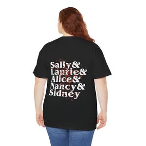 Può includere: T-shirt nero con testo bianco che recita "Sally & Laurie & Alice & Nancy & Sidney". Il testo è disposto verticalmente ed è accompagnato da disegni a spruzzi rossi. La maglietta è realizzata in un materiale morbido.