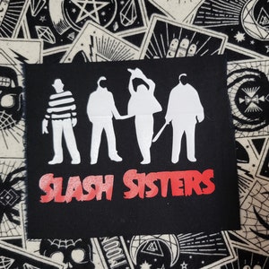 May include: Black fabric patch with white silhouettes of four figures, including Jason Voorhees, Michael Myers, Freddy Krueger, and Leatherface. The text "SLASH SISTERS" is in red below the figures.