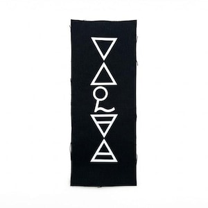 May include: A rectangular black fabric banner featuring a vertical arrangement of five white geometric symbols. The design includes two downward-pointing triangles, one upward-pointing triangle, a circular emblem, and a triangle with a horizontal line.