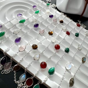 May include: A collection of silver chain bracelets with various gemstone teardrop pendants, including amethyst, green aventurine, rose quartz, tiger's eye, moonstone, red carnelian, malachite, and labradorite.