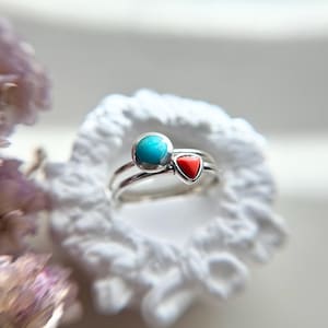 May include: A silver ring with a turquoise stone and a red heart-shaped stone.