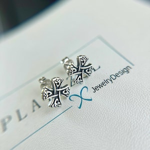 May include: A pair of silver earrings with a Celtic cross design. The earrings are on a white surface with the text "JewelryDesign" visible.