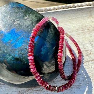 May include: A pink gemstone necklace with silver accents. The necklace is made of small, faceted beads and is strung on a silver chain.