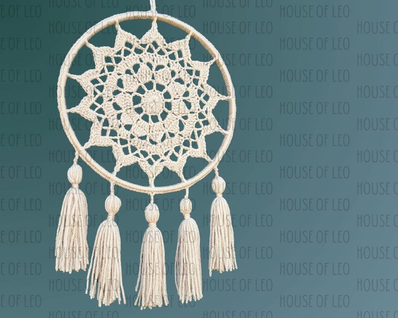 May include: A white crocheted dreamcatcher with a circular design and five tassels hanging from the bottom. The dreamcatcher is hanging against a teal background.