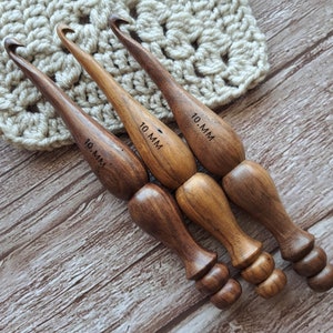 Op de afbeelding: Drie houten haaknaalden, elk met een maat van 10 mm gemarkeerd op de handgreep. De haaknaalden zijn bruin en hebben een gladde, gepolijste afwerking.