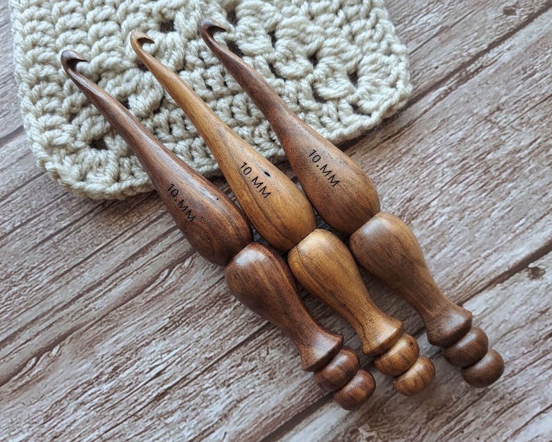 Op de afbeelding: Drie houten haaknaalden, elk met een maat van 10 mm gemarkeerd op de handgreep. De haaknaalden zijn bruin en hebben een gladde, gepolijste afwerking.