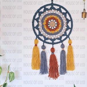 May include: A blue and beige crocheted dream catcher with a circular design and five tassels in shades of yellow, gray, and orange.