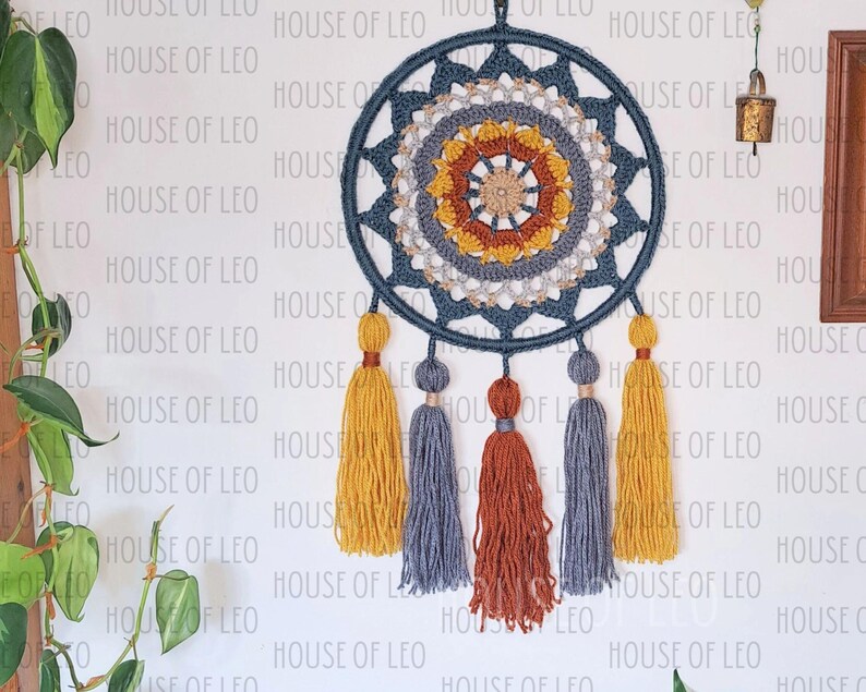 May include: A blue and beige crocheted dream catcher with a circular design and five tassels in shades of yellow, gray, and orange.