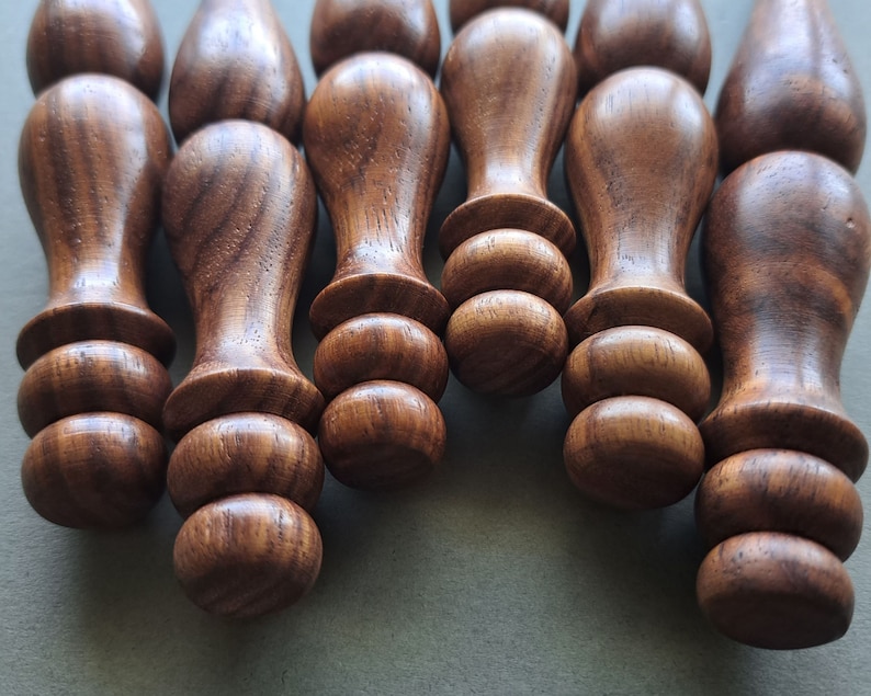 Op de afbeelding: Close-up van zeven houten pinnen met afgeronde uiteinden. De pinnen zijn in een rij gerangschikt, met de uiteinden van de pinnen naar de camera gericht. De pinnen zijn donkerbruin van kleur en hebben een gladde, gepolijste afwerking.