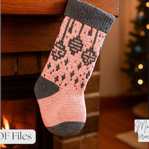 Peut inclure: Une chaussette de Noël faite à la main avec un motif de crochet mosaïque. La chaussette est principalement rose avec des accents gris au niveau du poignet, du talon et de la pointe. Le motif présente des ornements suspendus et des losanges. Les mots "PDF Files" sont visibles.