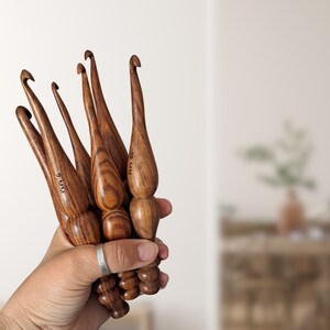 Op de afbeelding: Een set van vijf houten haaknaalden in verschillende maten. De haaknaalden zijn bruin en hebben een gladde, gepolijste afwerking. De maten van de haaknaalden zijn gemarkeerd op de handvatten: 9 mm, 10 mm, 12 mm, 15 mm en 10 mm.