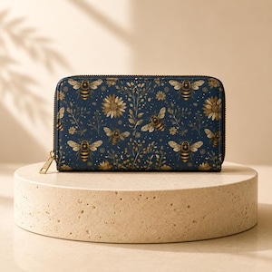 May include: A rectangular zip-around wallet featuring a dark navy blue background with a repeating pattern of golden-yellow bees, delicate wildflowers, and small white dots. The wallet has a gold-toned metal zipper pull attached to the side.