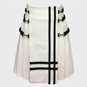 Może przedstawiać: Biały kilt z czarnymi akcentami. Kilt posiada czarne paski z metalowymi elementami i pionowe czarne paski. Poziome czarne paski znajdują się w pobliżu dołu. Tradycyjny element garderoby z nowoczesnym designem.