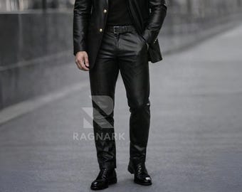May include: Black leather jacket with gold buttons, black leather pants, and black dress shoes. The outfit includes a black belt. The image shows a person wearing the outfit while standing on a gray surface. The brand name "RAGNARK" is visible.